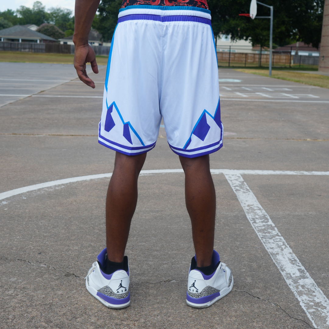 Man wearing white and blue reversible Rockies Shorts standing on an outdoor basketball court.